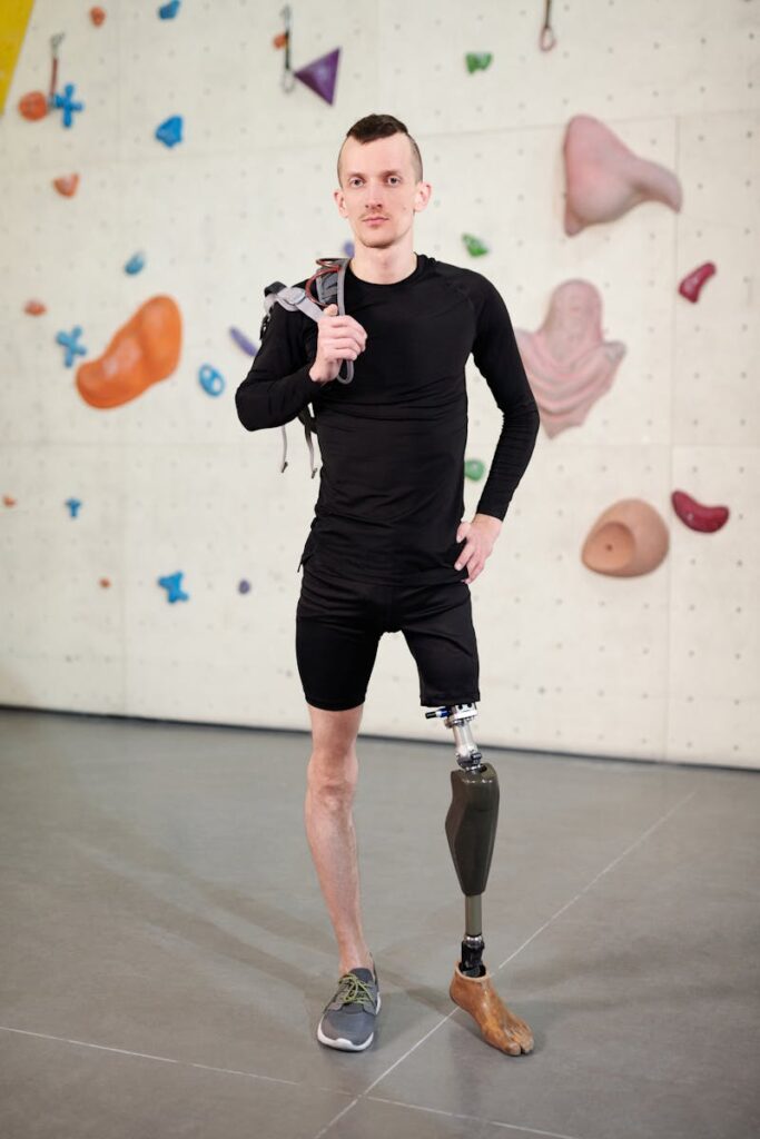 Young man with prosthetic leg confidently posing at indoor climbing gym, showcasing determination and strength.